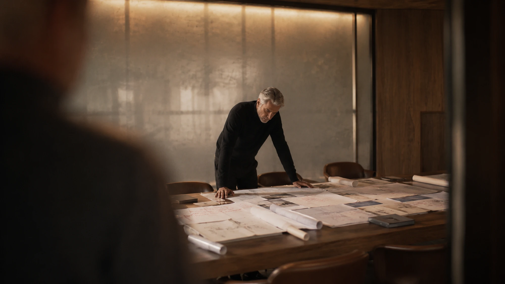 An architect reviewing drawings spread across a studio table.